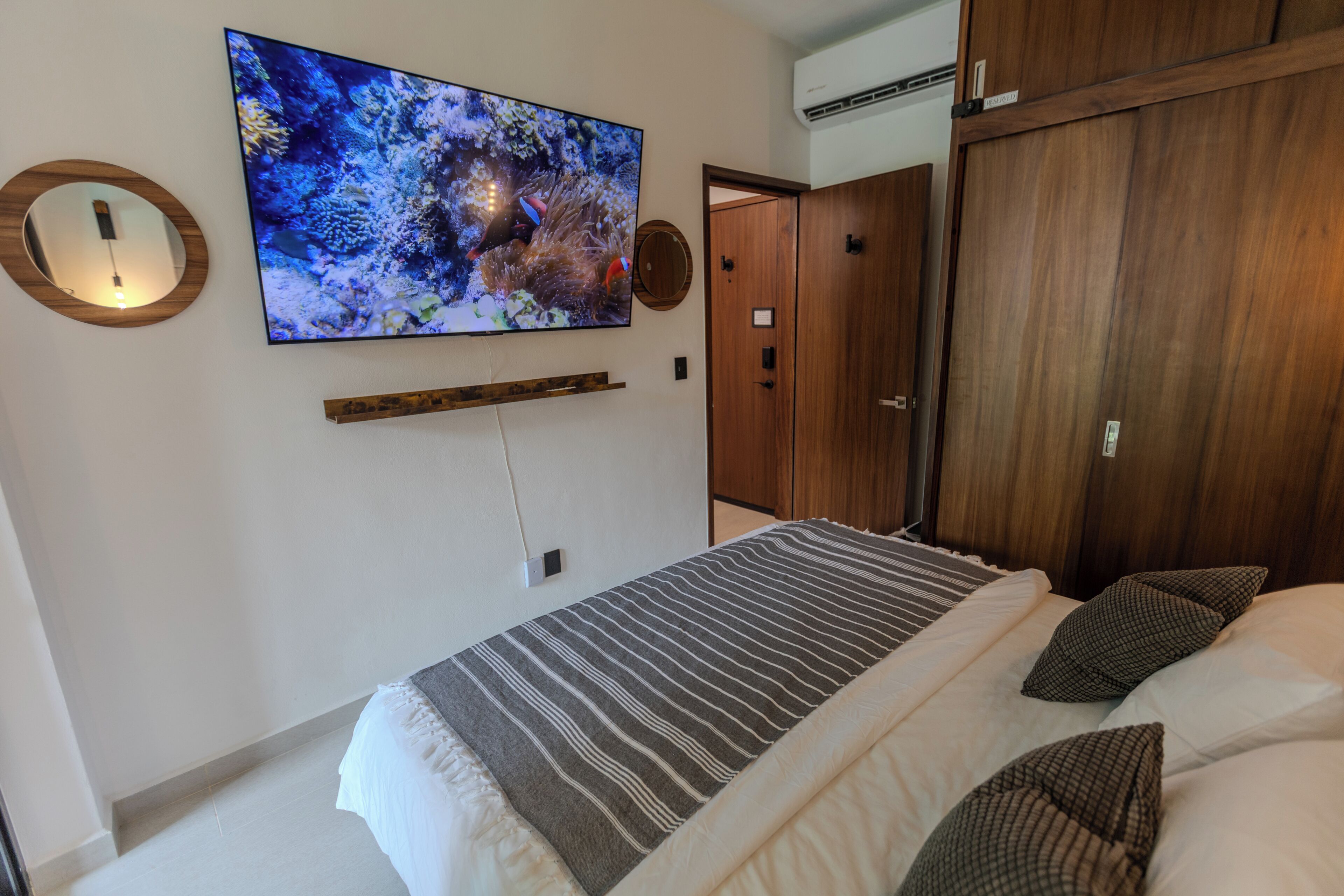 A bedroom with a bed, a mounted TV, a wooden wardrobe, and a door.