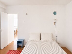 A bedroom with a bed, a nightstand, a lamp, and a door leading to another room. - Grand T2 lumineux • Gare St-Charles & Vieux-Port (Marseille)