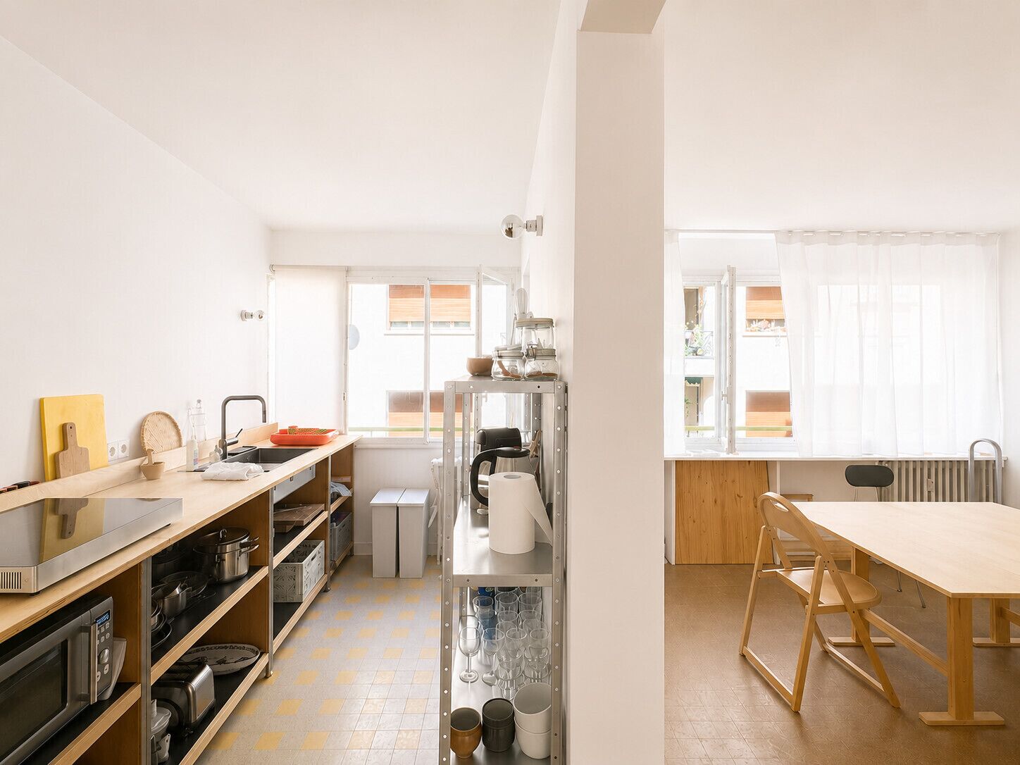 Una cocina con microondas, estufa y diferentes utensilios. Hay una mesa de comedor con sillas y una ventana con cortinas.