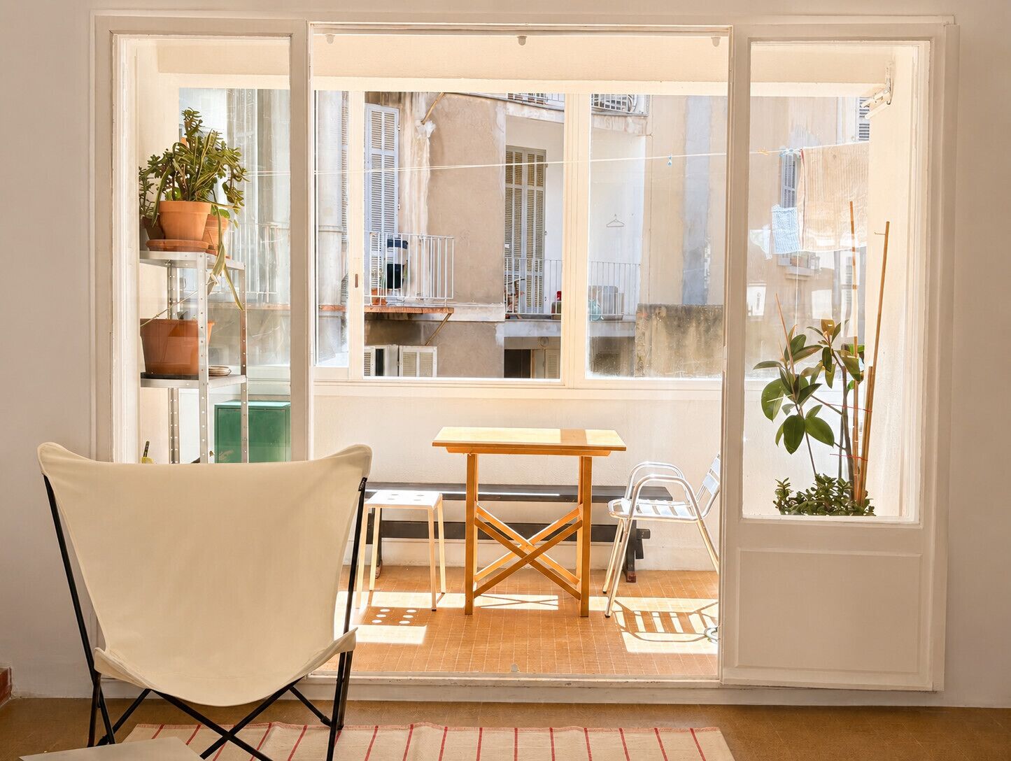 Een kamer met een stoel, een tafel en uitzicht door een glazen deur op een buitenbalkon met planten en een balustrade.