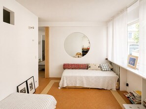 Quarto com cama, espelho redondo, janela e radiador.
