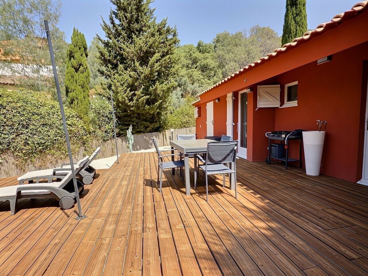 Une terrasse en bois avec une table et des chaises, un barbecue et des fauteuils de jardin.