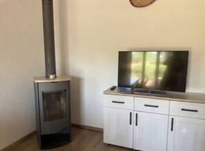Ein Zimmer mit Kaminofen, Fernseher auf einem Schrank und Wanduhr.