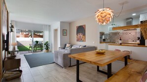 En moderne stue med en grå sofa, et træspisebord og et køkkenområde med mikroovn og et mønstret bagpanel.
