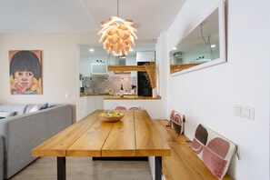 Cozinha moderna com mesa de jantar de madeira, luminária pendente e um quadro na parede.