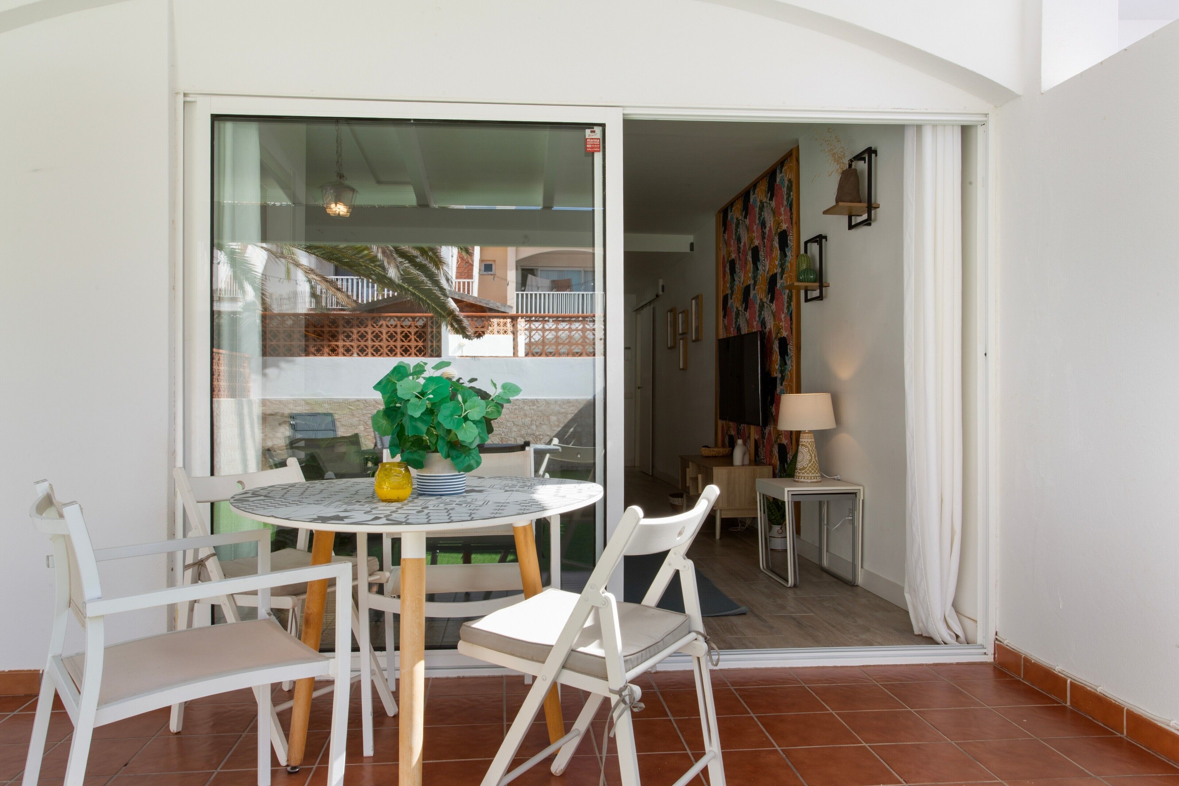 Un comedor con una mesa y sillas, una planta en maceta y vistas a un balcón con barandilla.