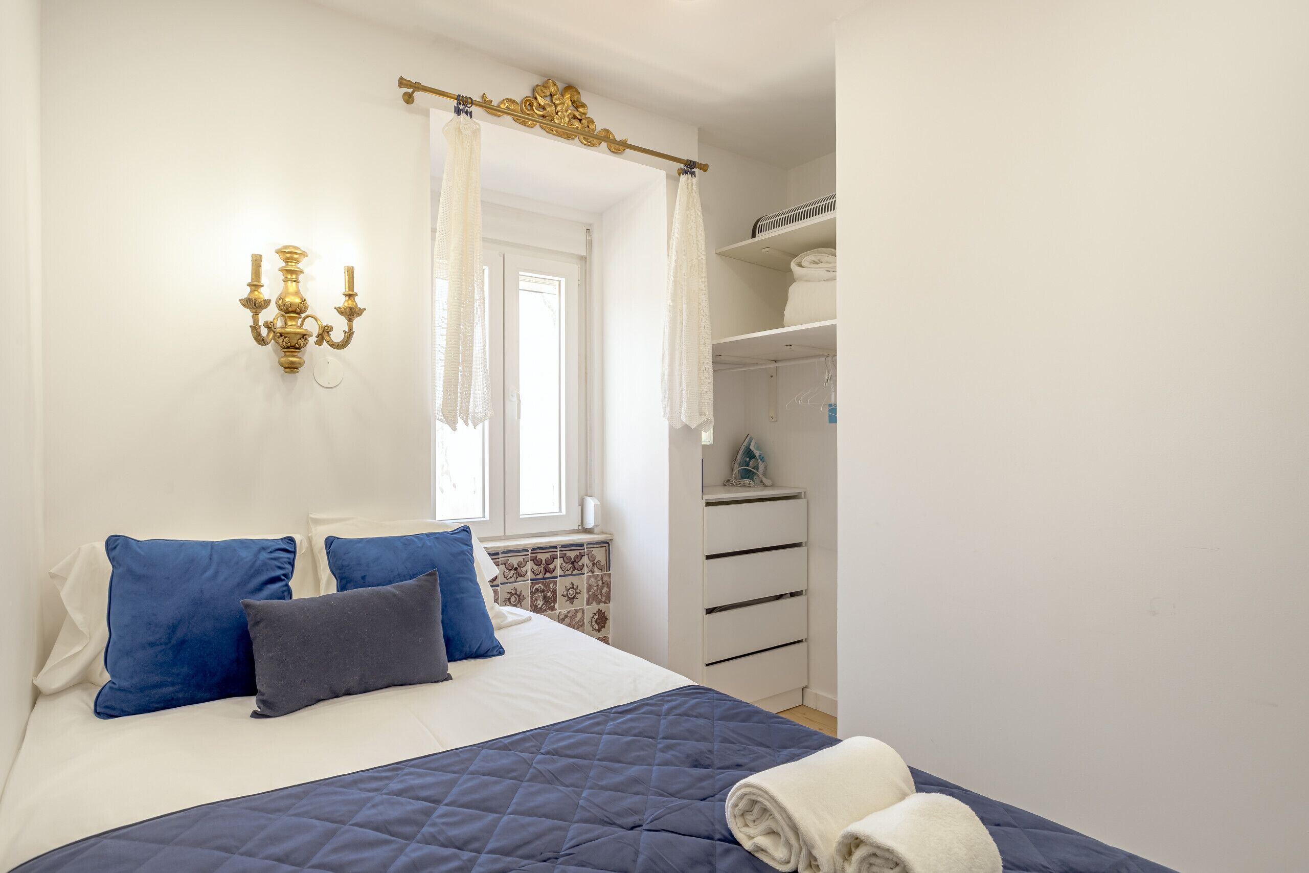 Une chambre à coucher avec un lit, des oreillers, une table de chevet, une armoire et une fenêtre avec des rideaux.