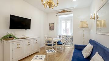 Un salon moderne doté d’un téléviseur à écran plat, d’un canapé bleu, d’une table à manger avec des chaises et d’un lustre.