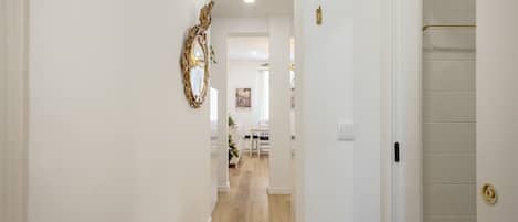 A hallway with a wooden floor, white walls, and a door with a gold handle.