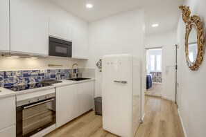 Eine kleine Küche mit weißen Schränken, einem eingebauten Backofen, einer Edelstahl-Dunstesse und einem Kühlschrank.