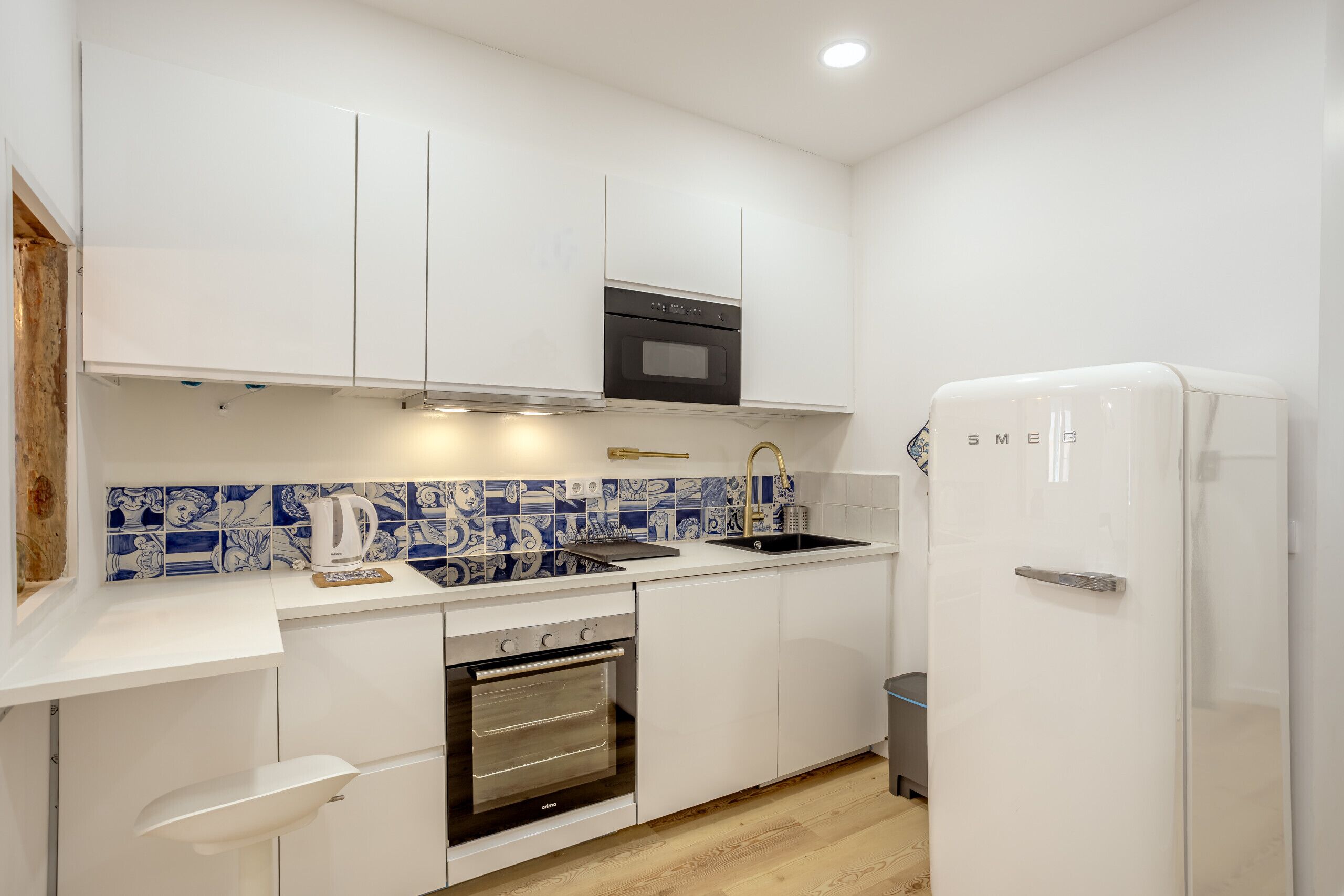 Una cucina compatta con mobili bianchi, forno nero, frigorifero bianco e zoccolo di piastrelle blu.