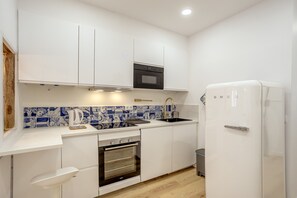 Una cucina compatta con mobili bianchi, forno nero, frigorifero bianco e zoccolo di piastrelle blu.