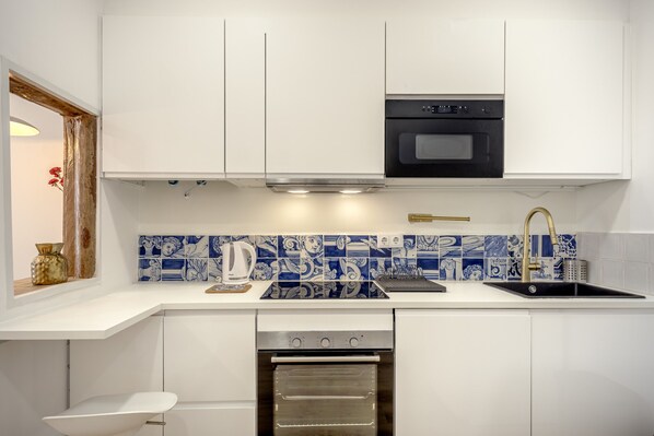 A kitchen with white cabinets, a black oven, a stainless steel range hood, a sink with a gold faucet, and blue and white patterned backsplash tiles. - Bairro Alto Stylish II by Homing (Lisbon)