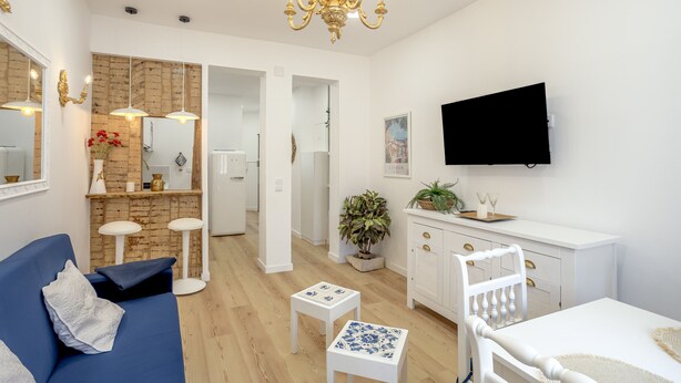 A modern living room with a blue sofa, white coffee table, and a dining area with a white cabinet and a TV mounted on the wall. - Bairro Alto Stylish II by Homing (Lisbon)