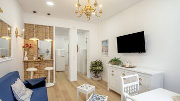 Un salon moderne avec un canapé bleu, une table basse blanche et un coin repas comprenant un buffet blanc et un téléviseur fixé au mur.