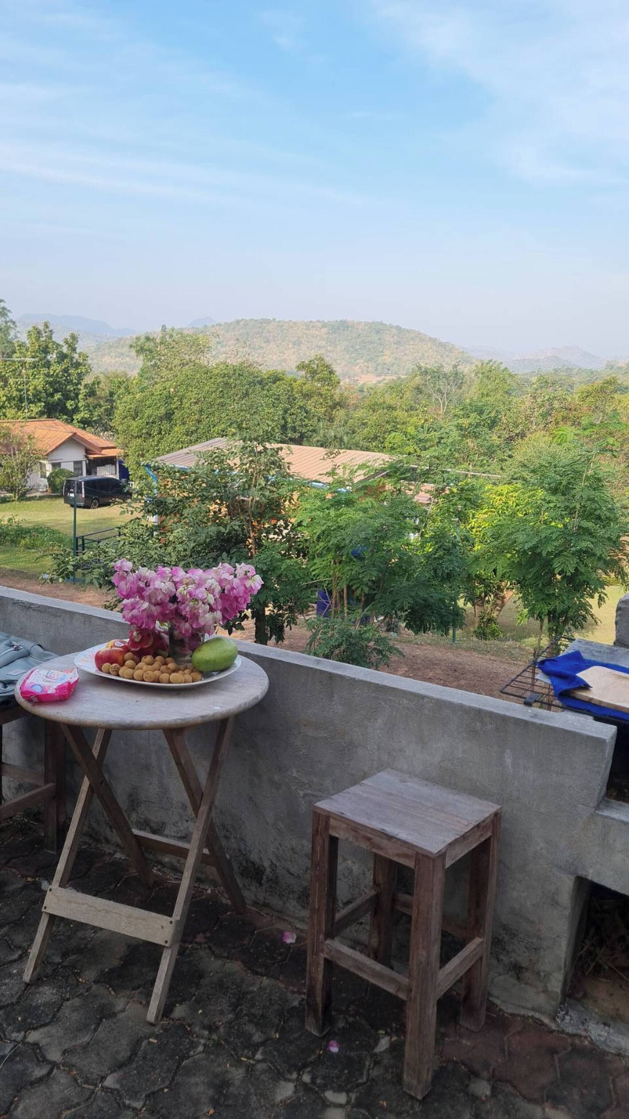 A balcony with a table, a small stool, and a vase of flowers.