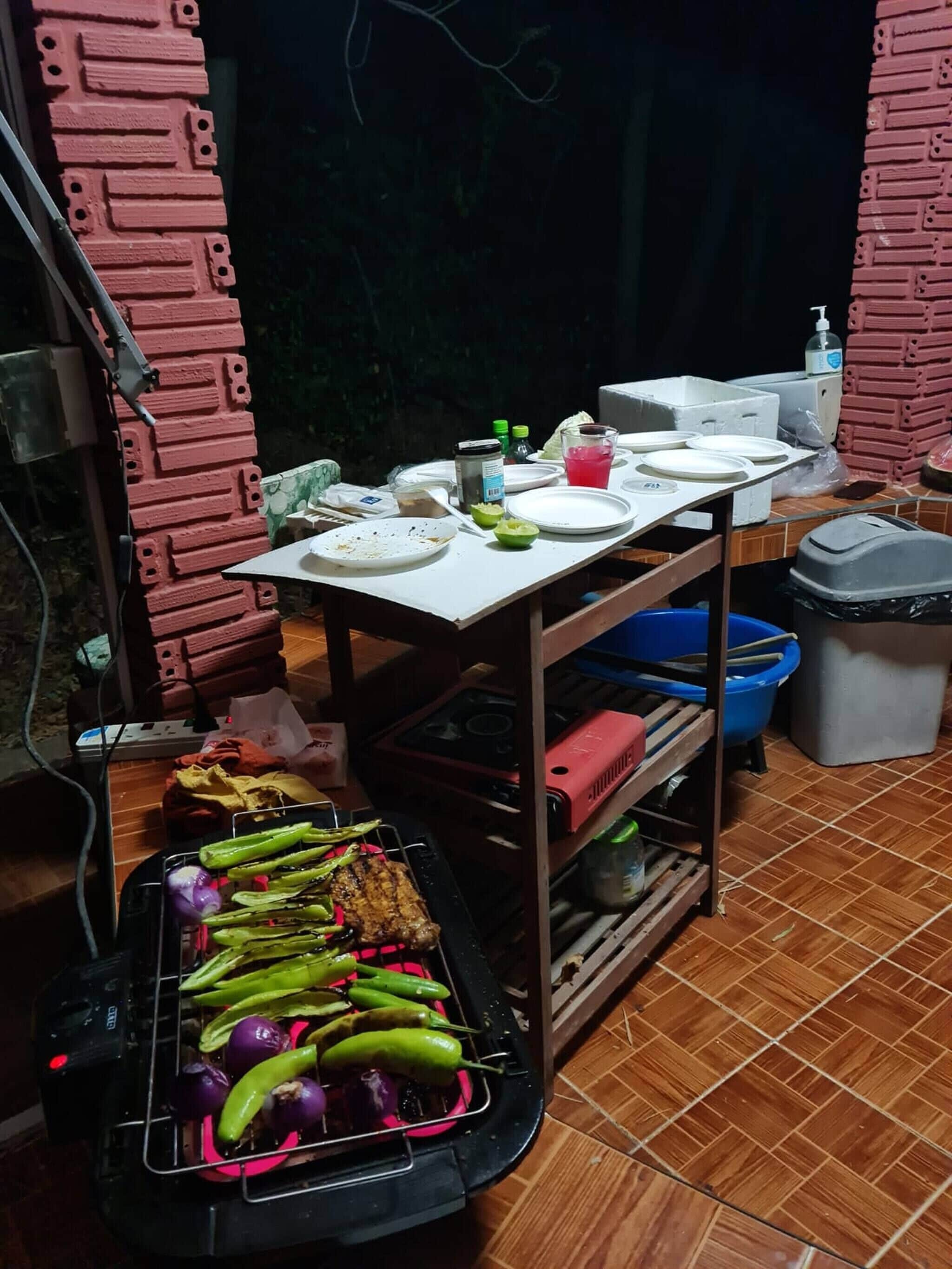 A kitchen area with a grill, a table with plates and condiments, and a trash bin.