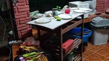 A kitchen area with a grill, a table with plates and condiments, and a trash bin.