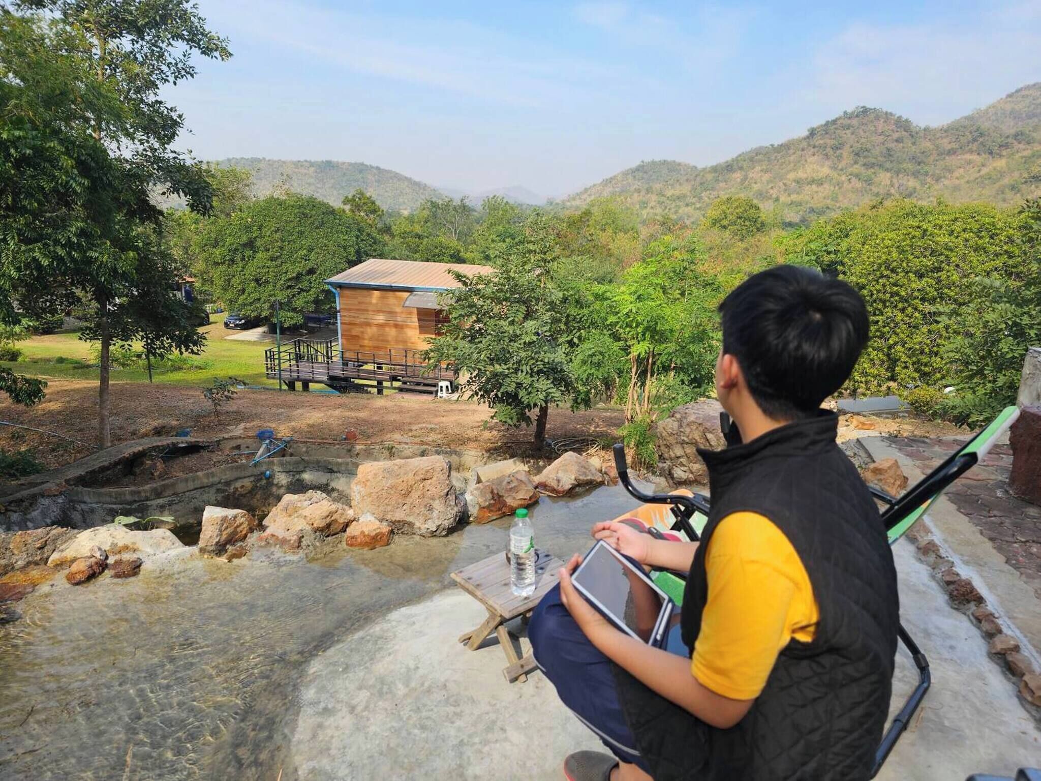 A person sitting by a clear water feature with a wooden deck and a building in the background.