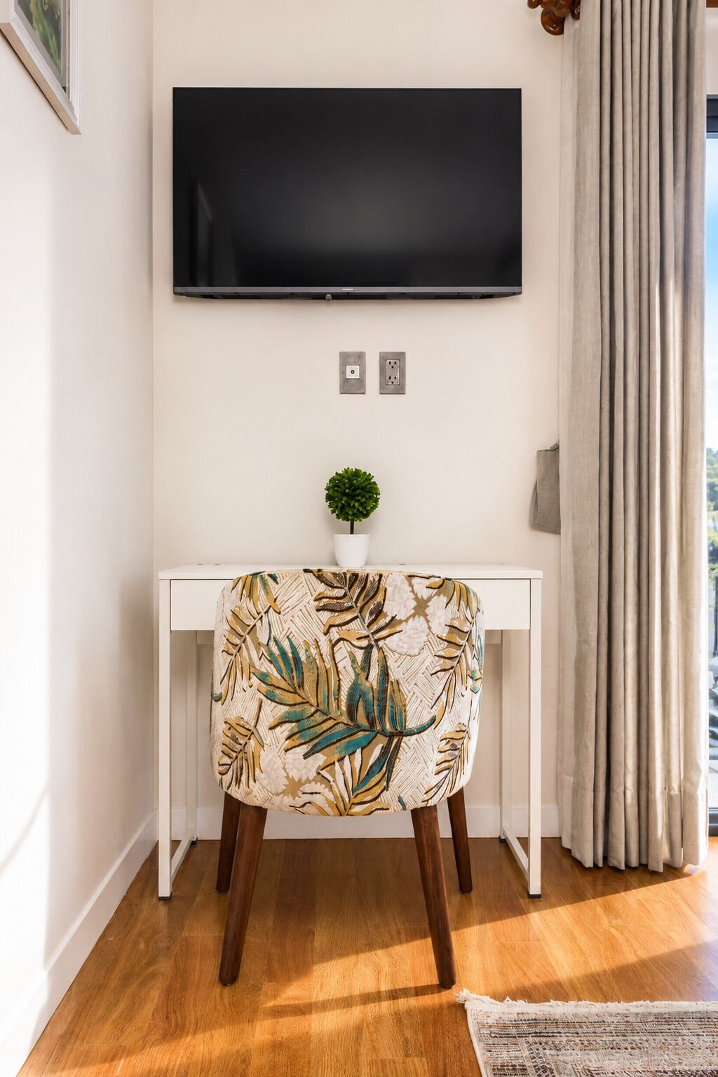 A modern living room with a white console table, a flat-screen TV mounted above it, a small potted plant, and a chair with a leaf-patterned upholstery.