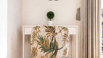 A modern living room with a white console table, a flat-screen TV mounted above it, a small potted plant, and a chair with a leaf-patterned upholstery.
