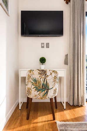 A modern living room with a white console table, a flat-screen TV mounted above it, a small potted plant, and a chair with a leaf-patterned upholstery. - Breathtaking view in modern neighborhood of La Paz! (La Paz)