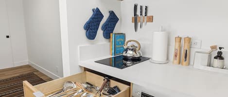 A modern kitchen with a built-in dishwasher, a kettle, and a variety of utensils in a wooden drawer.