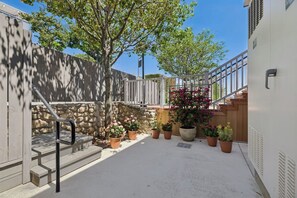 A courtyard with a stone wall, potted plants, and a staircase leading to an upper level.