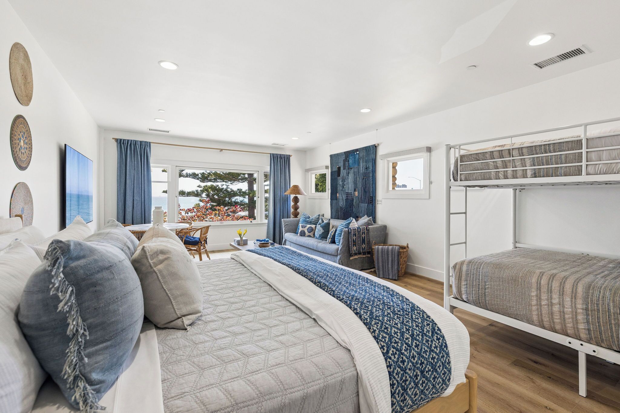 A modern bedroom with a bunk bed, a sofa, and a dining area with a view.