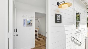 En hall med en vit dörr, en väggmonterad lampa och en inramad skylt med text.