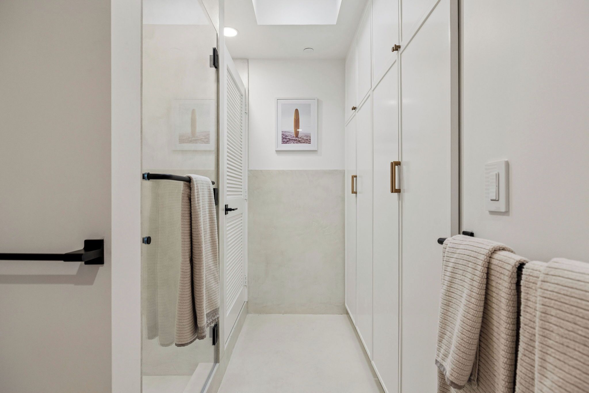A narrow hallway with a shower area on the left, a framed picture on the wall, and a set of cabinets on the right.
