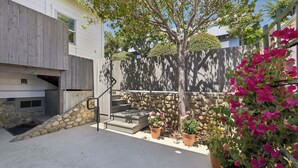 A residential backyard with a stone wall, a wooden fence, and potted plants. - The Big Yellow House Lofts by the beach (Summerland)