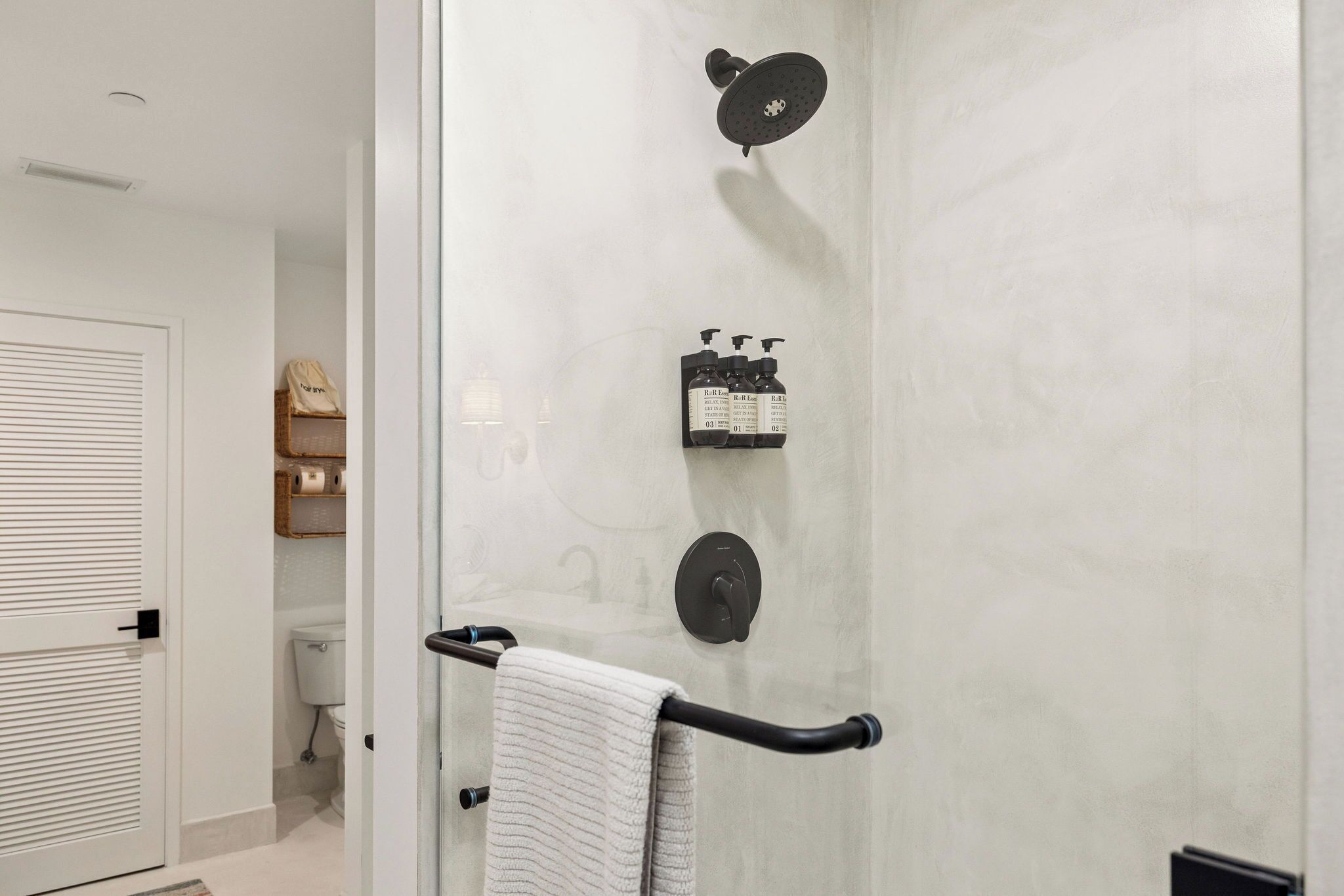 Ein modernes Badezimmer mit Duschkabine aus Glas, einem Handtuchhalter und einer Toilette im Hintergrund.