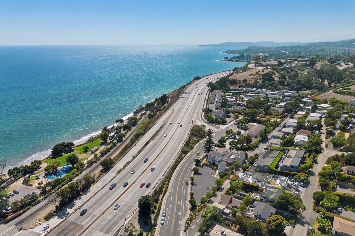 Eine Küstenstraße mit mehreren Fahrstreifen, angrenzenden Wohngebieten und einem Strand.