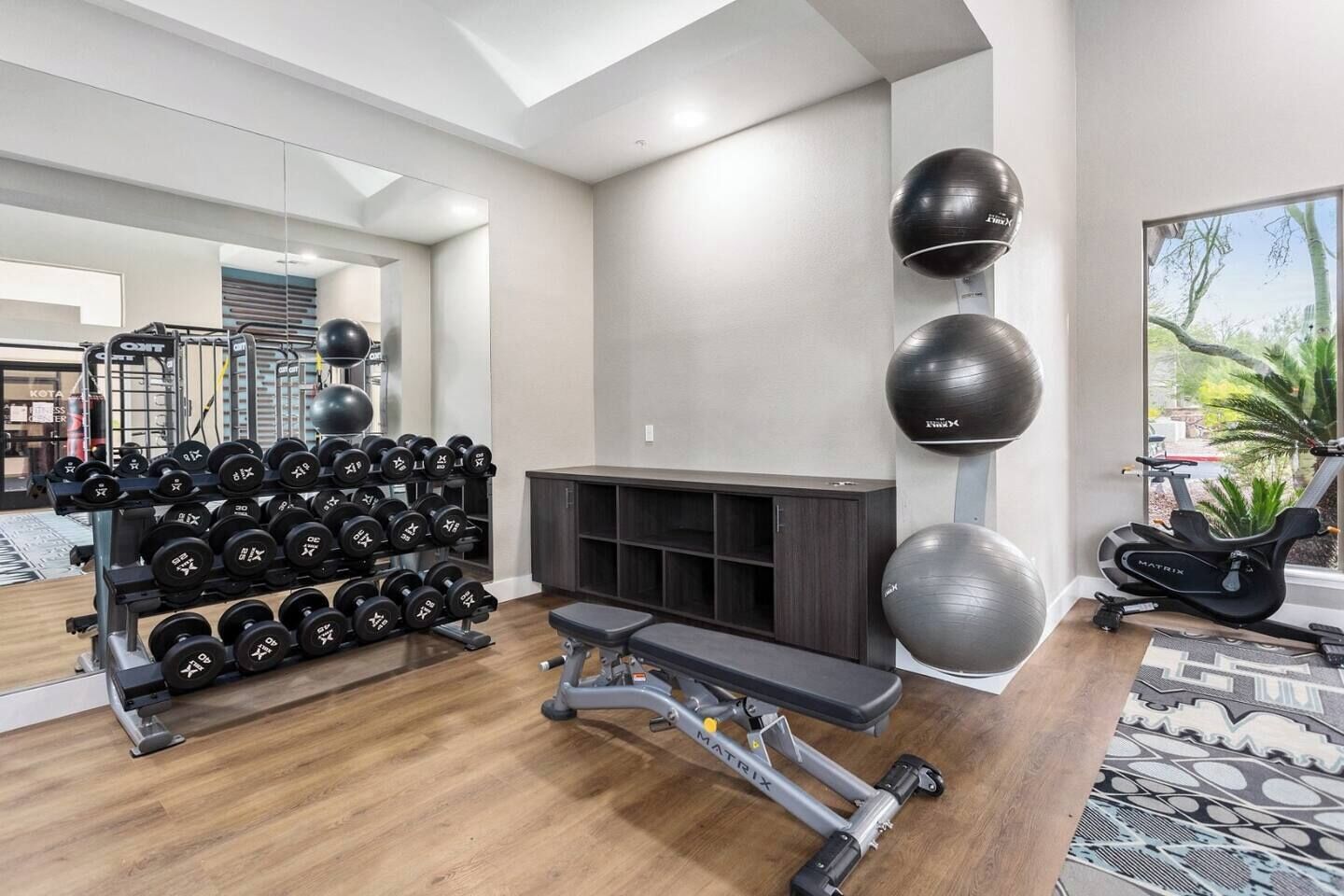 Ein Fitnessraum mit Trainingsgeräten, einer Bank und Blick ins Freie.