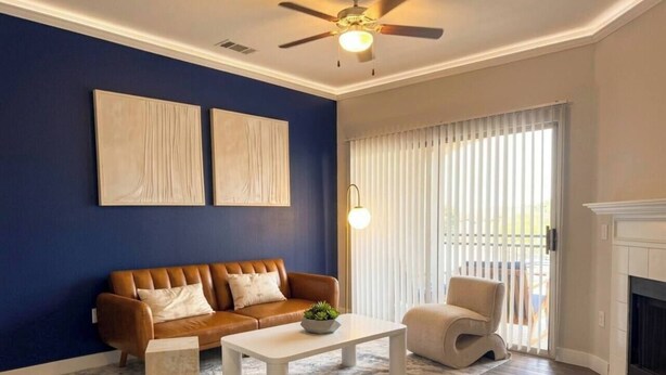 A living room with a brown leather sofa, a white coffee table, a beige armchair, a fireplace, and a ceiling fan. - Scottsdale Stay  Near Spring Training Games (Scottsdale)