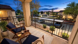 A balcony with a seating area, a table with a bottle and glasses, and a view of a parking area and buildings. - Scottsdale Stay  Near Spring Training Games (Scottsdale)