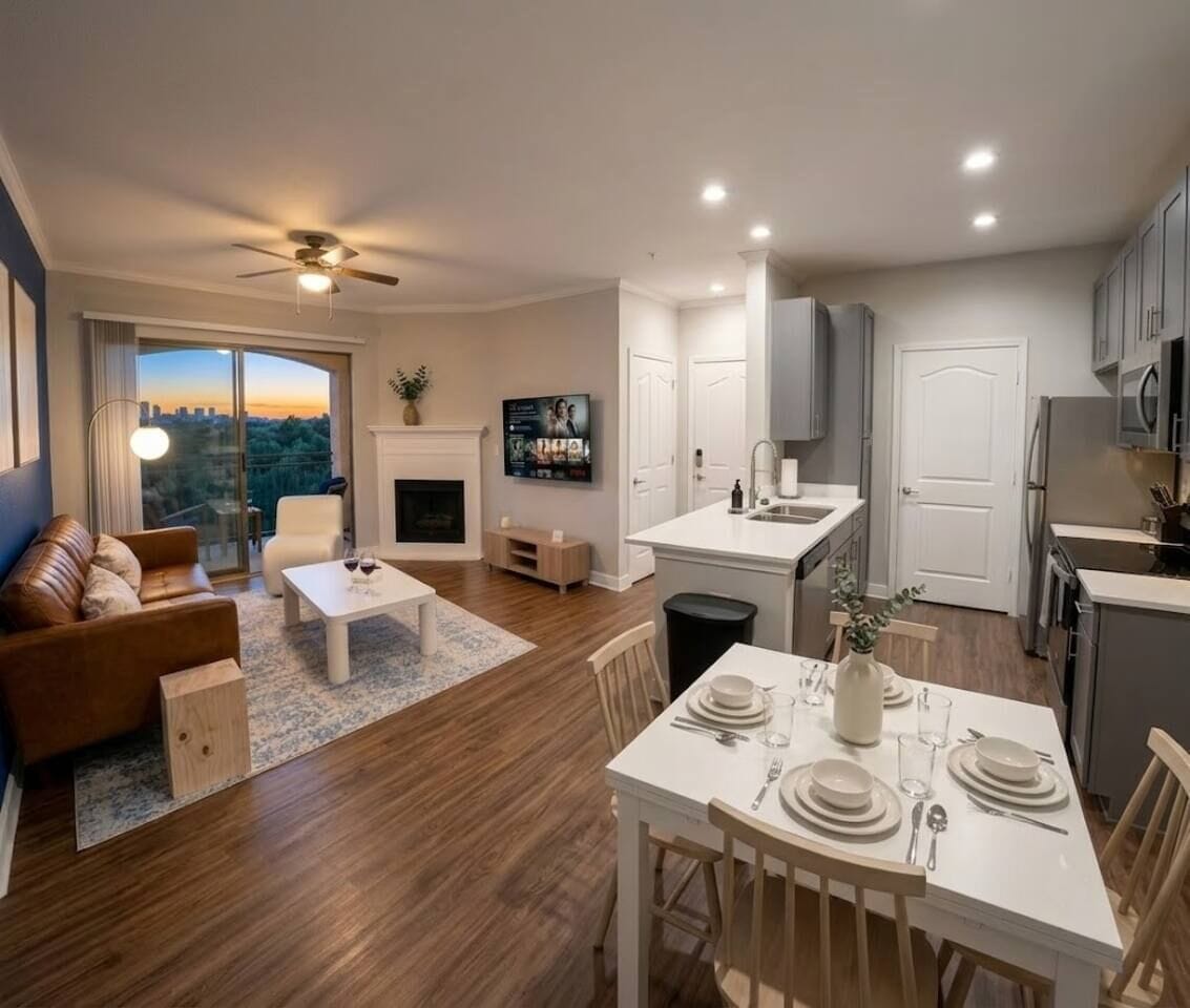 A modern living room with a sofa, coffee table, and TV, connected to a kitchen with a dining area.