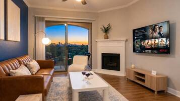 A living room with a sofa, coffee table, fireplace, TV, and a view through a glass door.