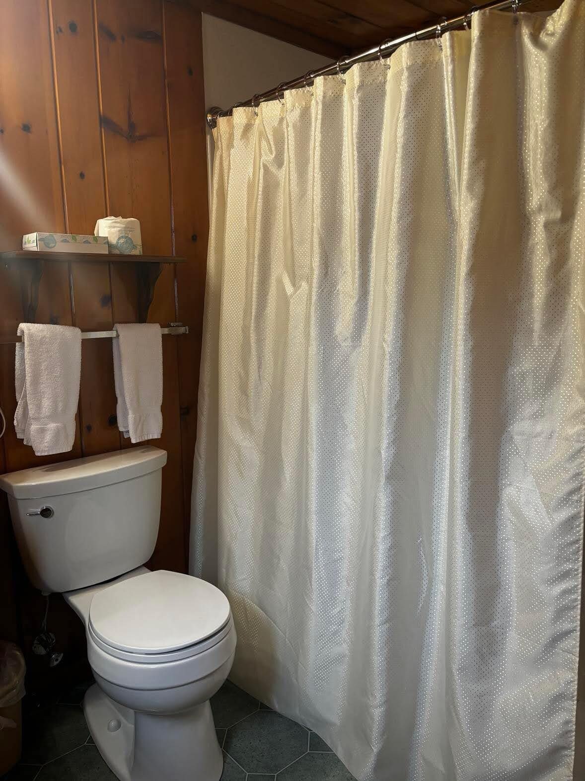 Un baño con inodoro, cortina de ducha y un estante con toallas.