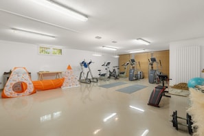 Ein Fitnessstudio mit unterschiedlichen Trainingsgeräten, darunter Laufbänder, Ergometer und ein Rudergerät.