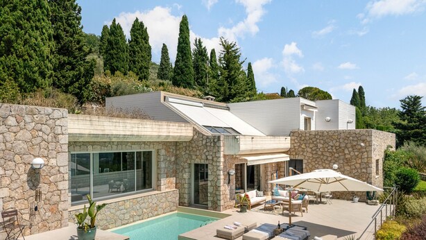 Uma casa moderna com piscina, paredes de pedra e um alpendre com cadeiras de descanso.