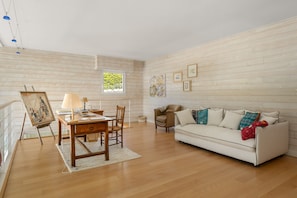 Ein geräumiges Wohnzimmer mit Holzboden, einem weißen Sofa, einem Holztisch mit Lampe und einem Bild an der Wand.