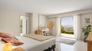 Quarto com cama, mesa de cabeceira e vista para o exterior.