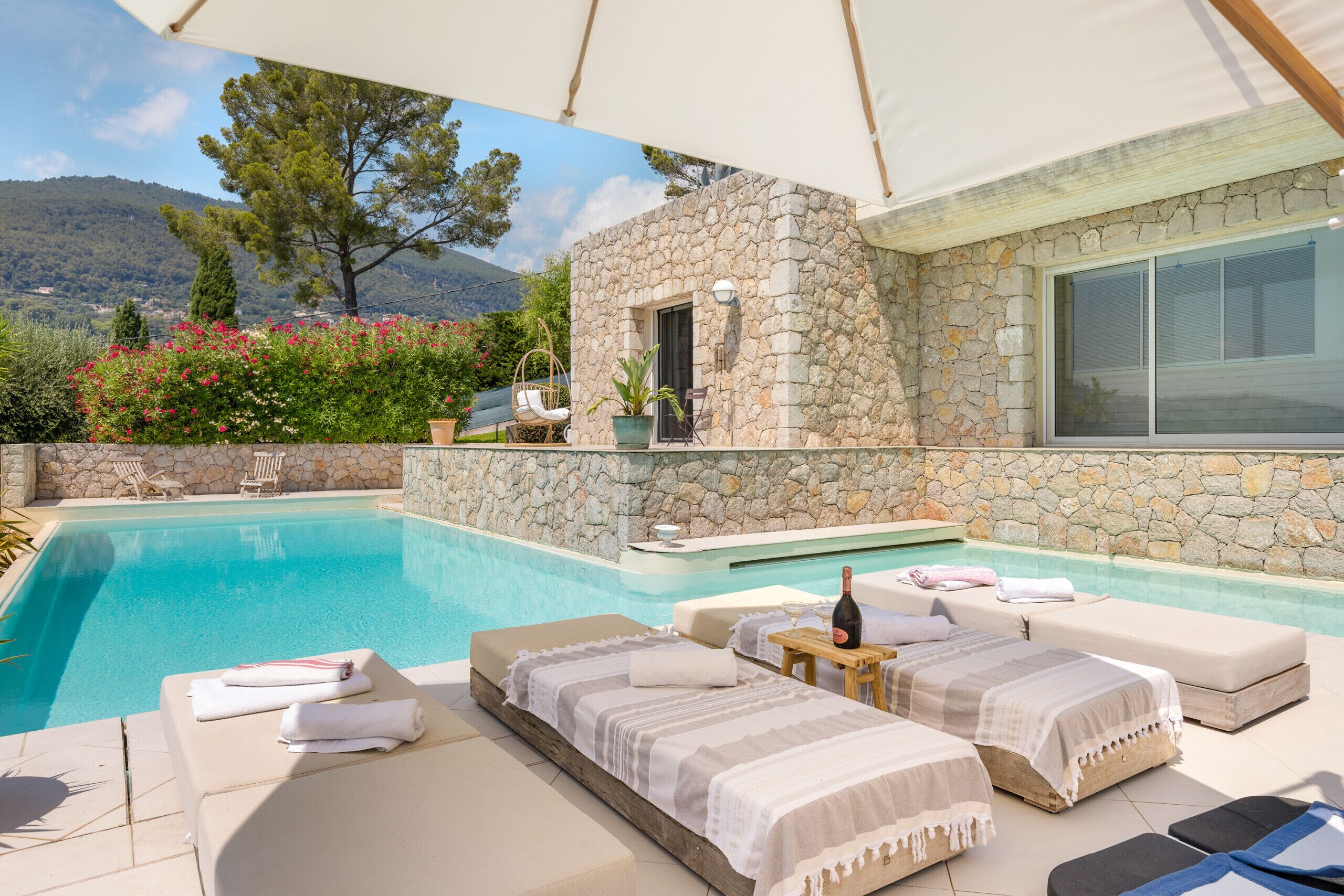 A poolside area with lounge chairs, a stone wall, and a view of the mountains.