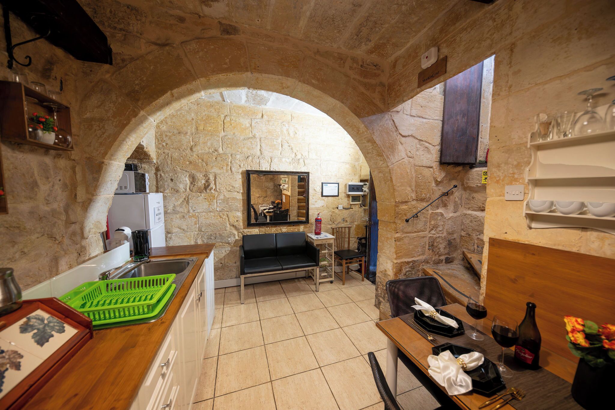 A stone-walled kitchen with a wooden counter, a sink, and a dining area with a table set for two.