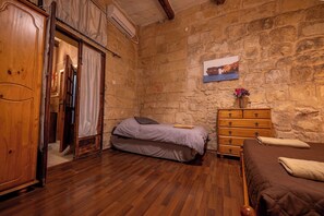 A bedroom with a stone wall, wooden furniture, a bed, a dresser, and a painting. - 3 Cities Maison: Terraced House of Character close to Valletta (Bormla)