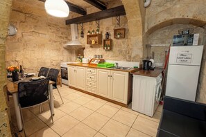 Een keuken met stenen muren, houten kastjes, een eethoek met stoelen en een koelkast met een 'HOUD HET GEBIED REIN' bord.