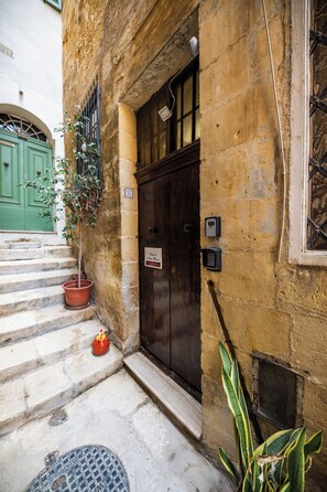 A building entrance with a wooden door, a potted plant, and a sign indicating the property name. - 3 Cities Maison: Terraced House of Character close to Valletta (Bormla)
