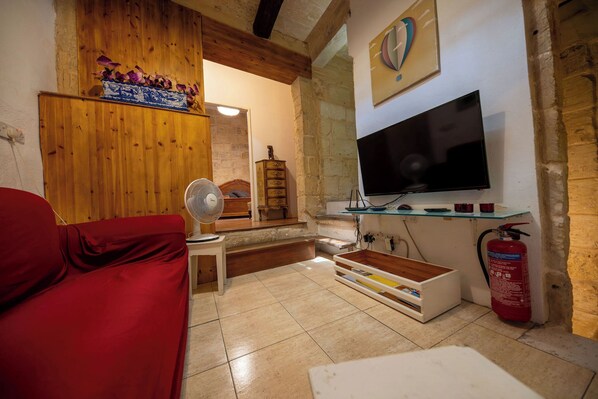 Een gezellige woonkamer met een rode bank, een houten plafond, een televisie en een brandblusser.